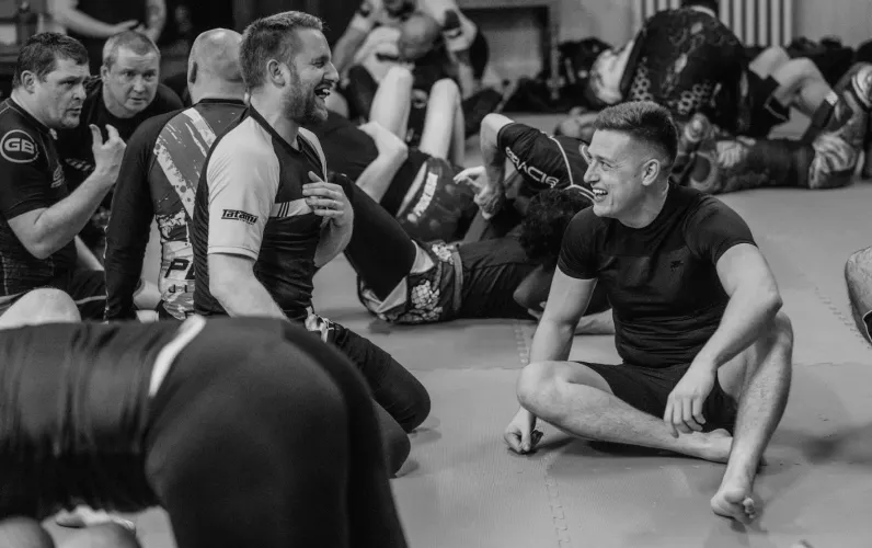 Two Jiu-Jitsu students sit together on the mats discussing BJJ techniques.