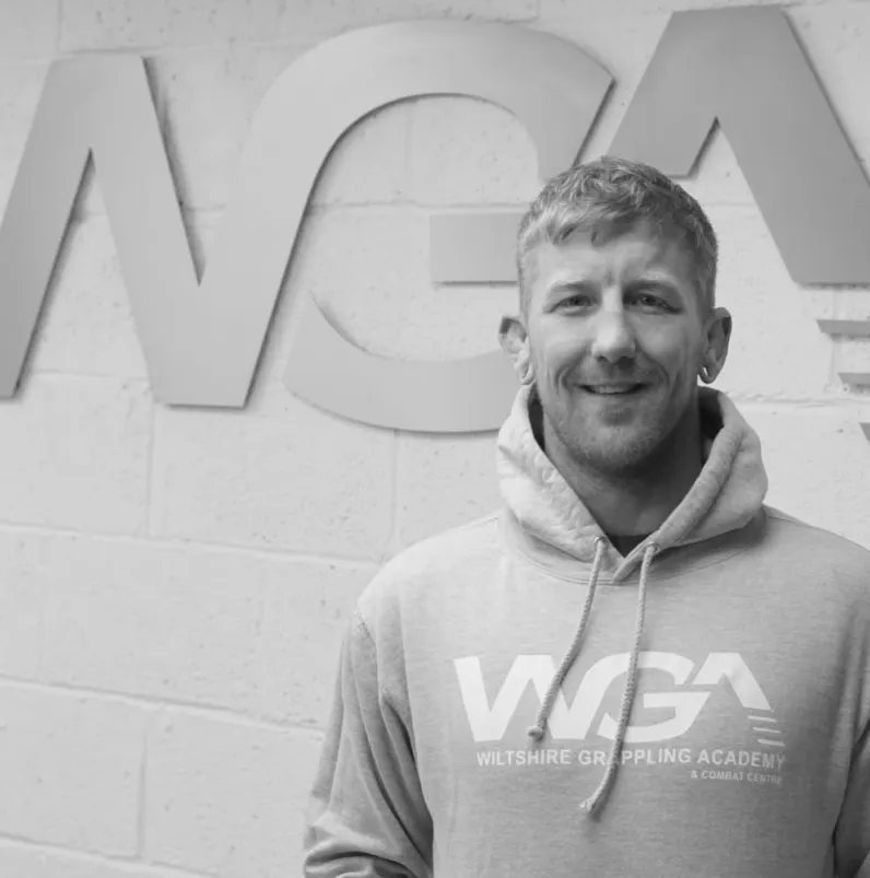 Coach Marc stands in front of the Wiltshire Grappling Academy logo.